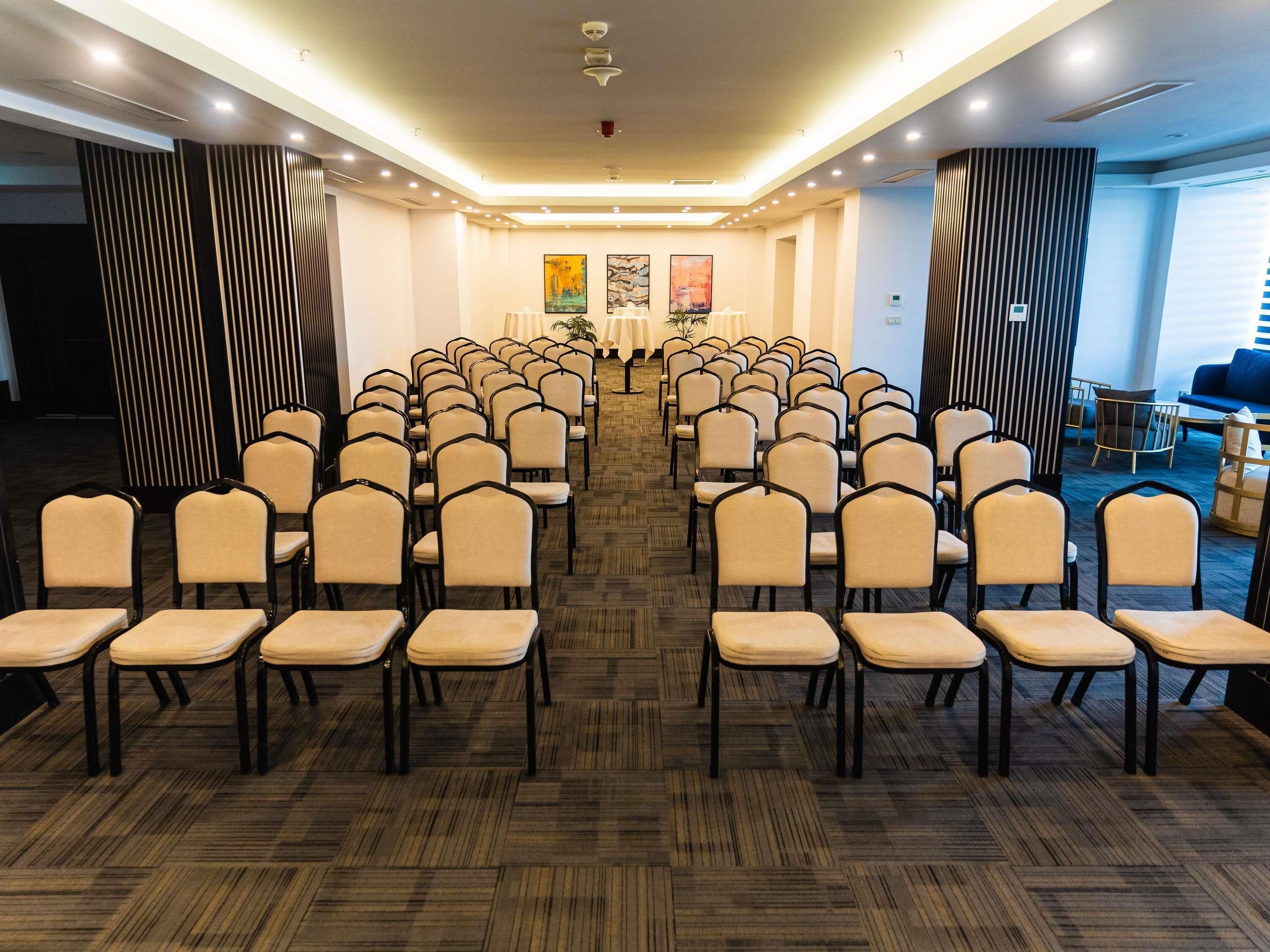Ein Konferenzraum mit Reihen von Stühlen, einem gemusterten Teppich und einer Decke mit eingelassenen Leuchten.