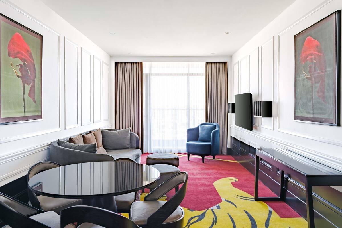 A modern hotel room with a sofa, armchairs, a dining table, and a TV.