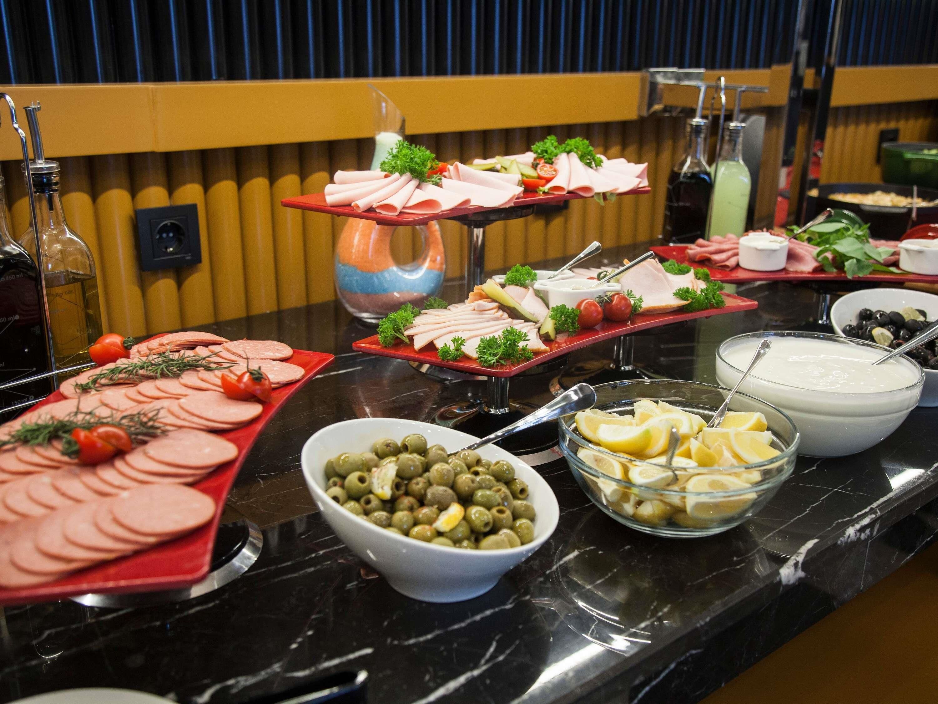 A buffet table with various food items including sliced meats, olives, and lemon slices.