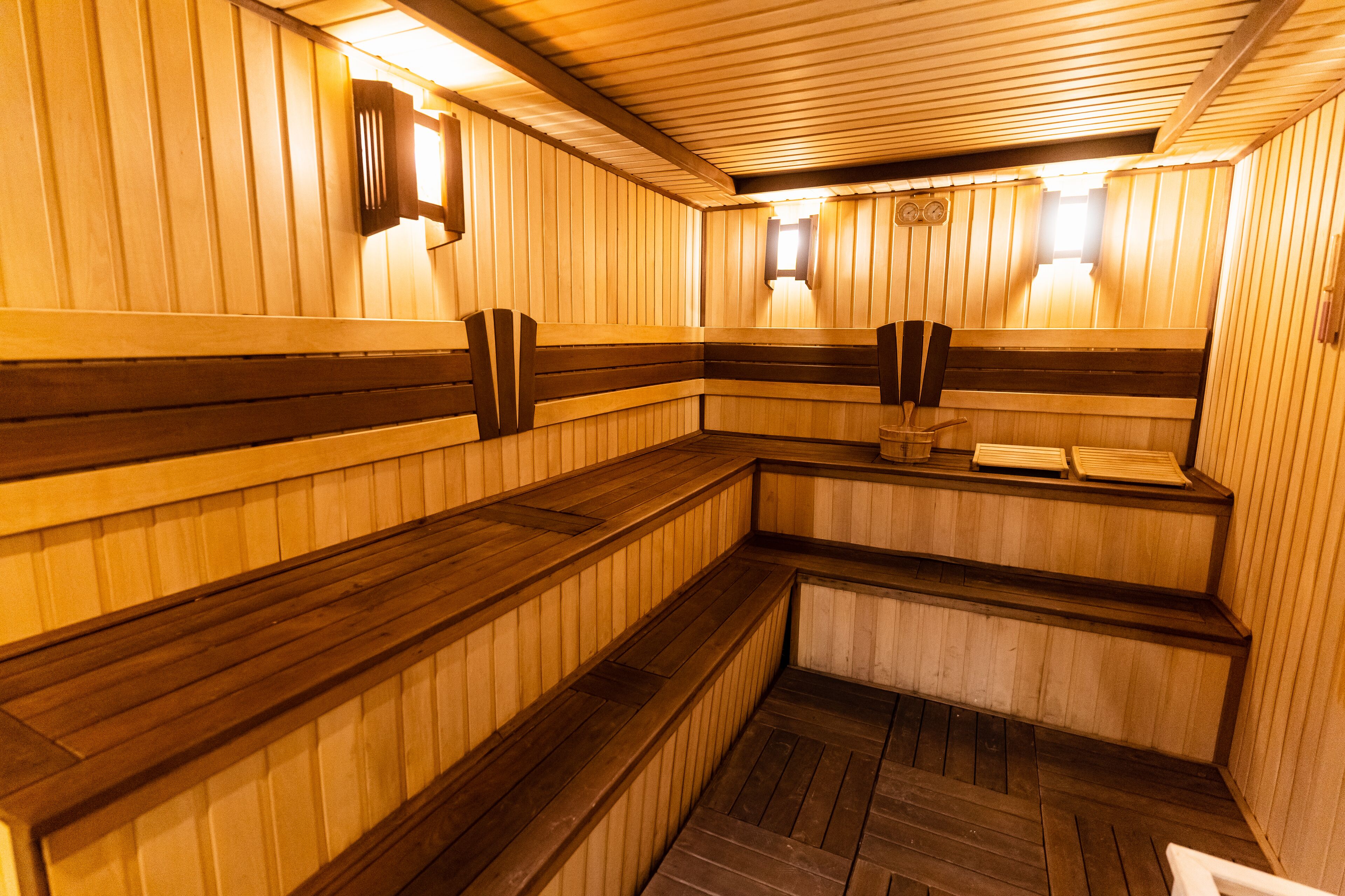 A sauna with wooden benches and walls, a clock, and a small window.