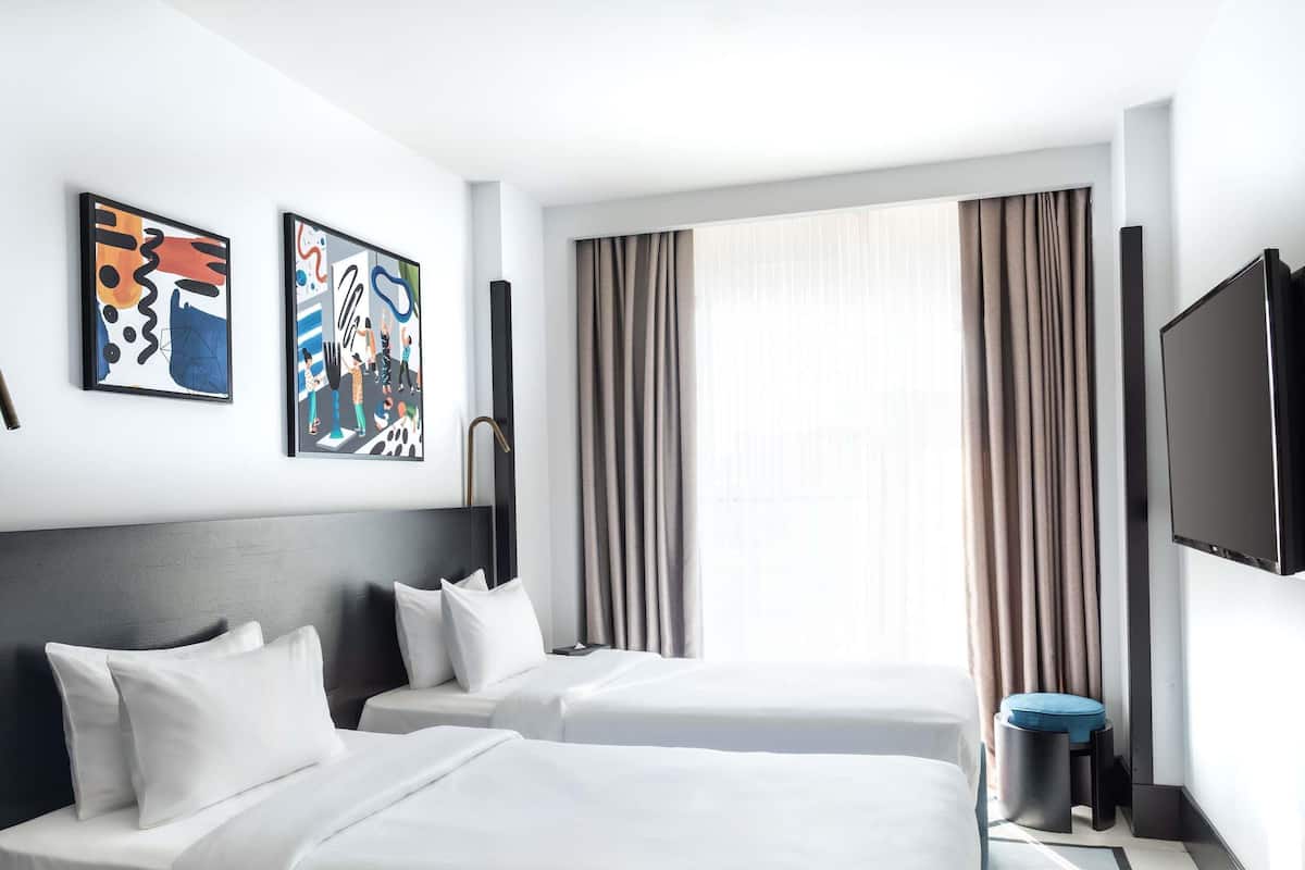 A hotel room with two beds, a TV, and abstract art on the wall.