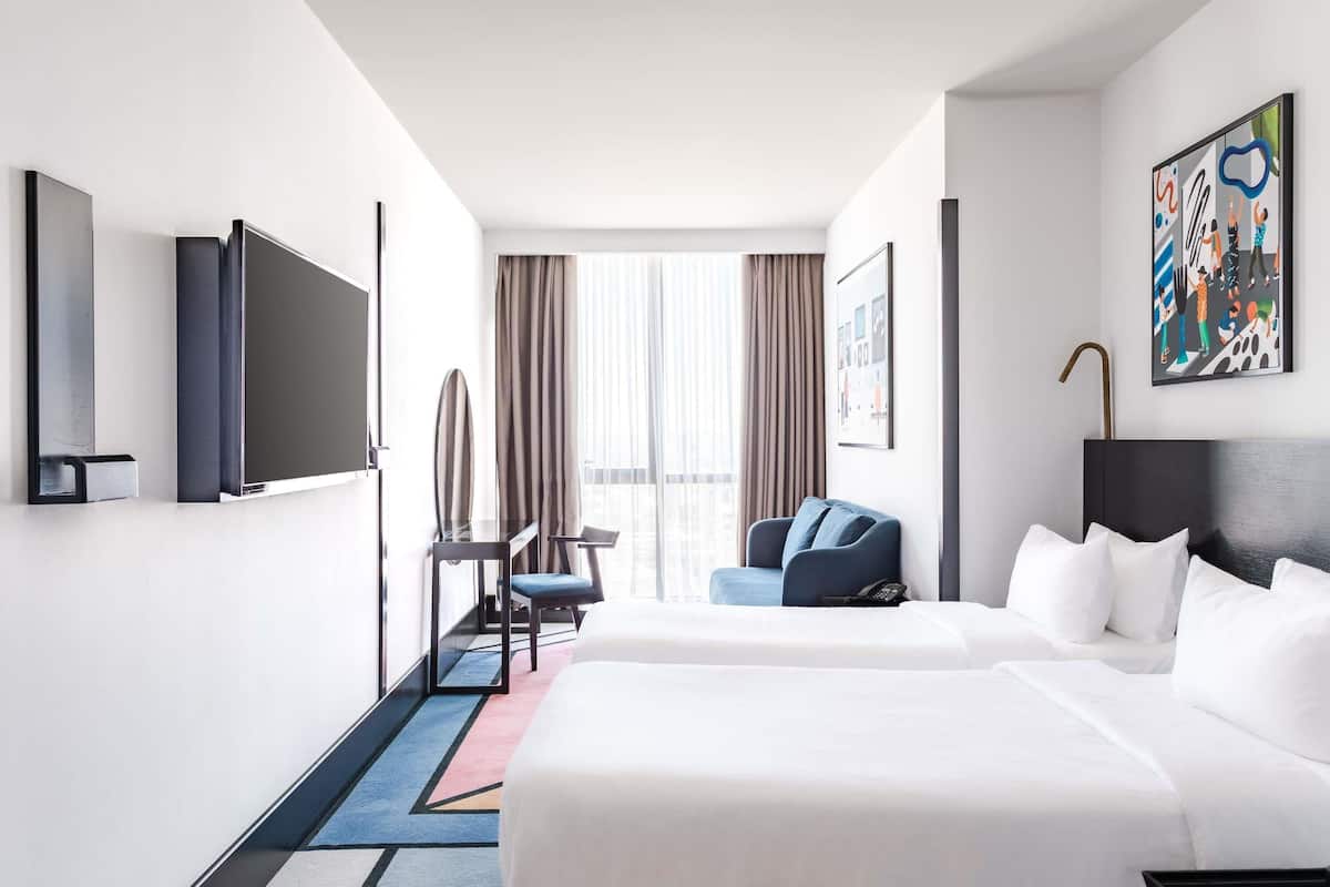 A hotel room with two beds, a desk, a chair, a TV, and a painting on the wall.