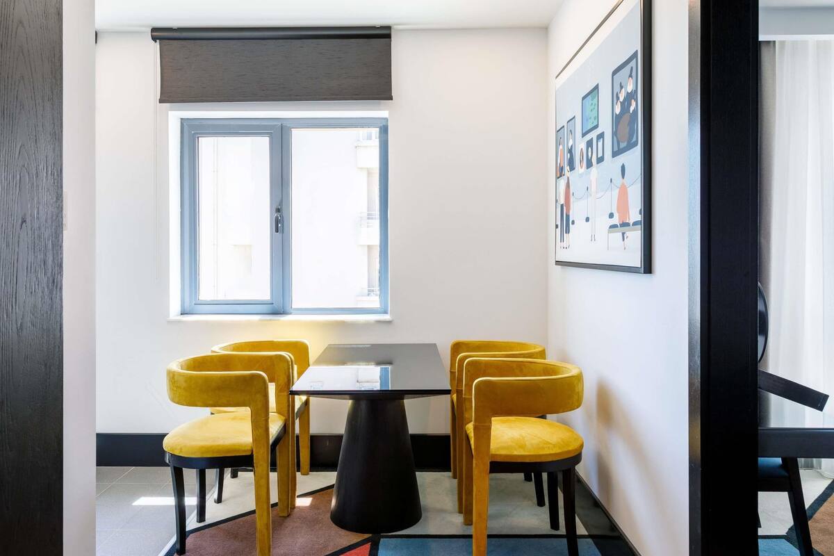 A room with a table, four chairs, a window, and a framed picture on the wall.
