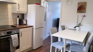 A modern kitchen with white cabinetry, a built-in oven, a refrigerator, and a dining area with a white table and grey chairs. - Modern 3 bedrooms house with 6 guests (Sheffield)