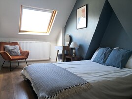 Un dormitorio con cama, una silla, un escritorio, una lámpara y una ventana.