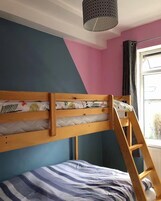 Una cama litera con escalera de madera, una ventana con cortinas y una lámpara en el techo.