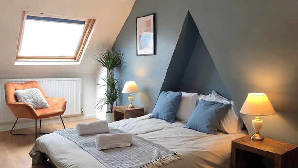 A bedroom with a bed, two bedside tables with lamps, a chair, a window, and a plant. - Modern 3 bedrooms house with 6 guests (Sheffield)