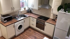 A compact kitchen with white cabinets, a microwave, a washing machine, an oven, and a refrigerator. - Modern 3 bedrooms house with 6 guests (Sheffield)