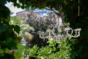 Un lustre à plusieurs bras et doté d’une pièce centrale, le tout entouré de verdure.