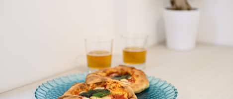 Two pizzas on a blue glass plate with two glasses of beer in the background.