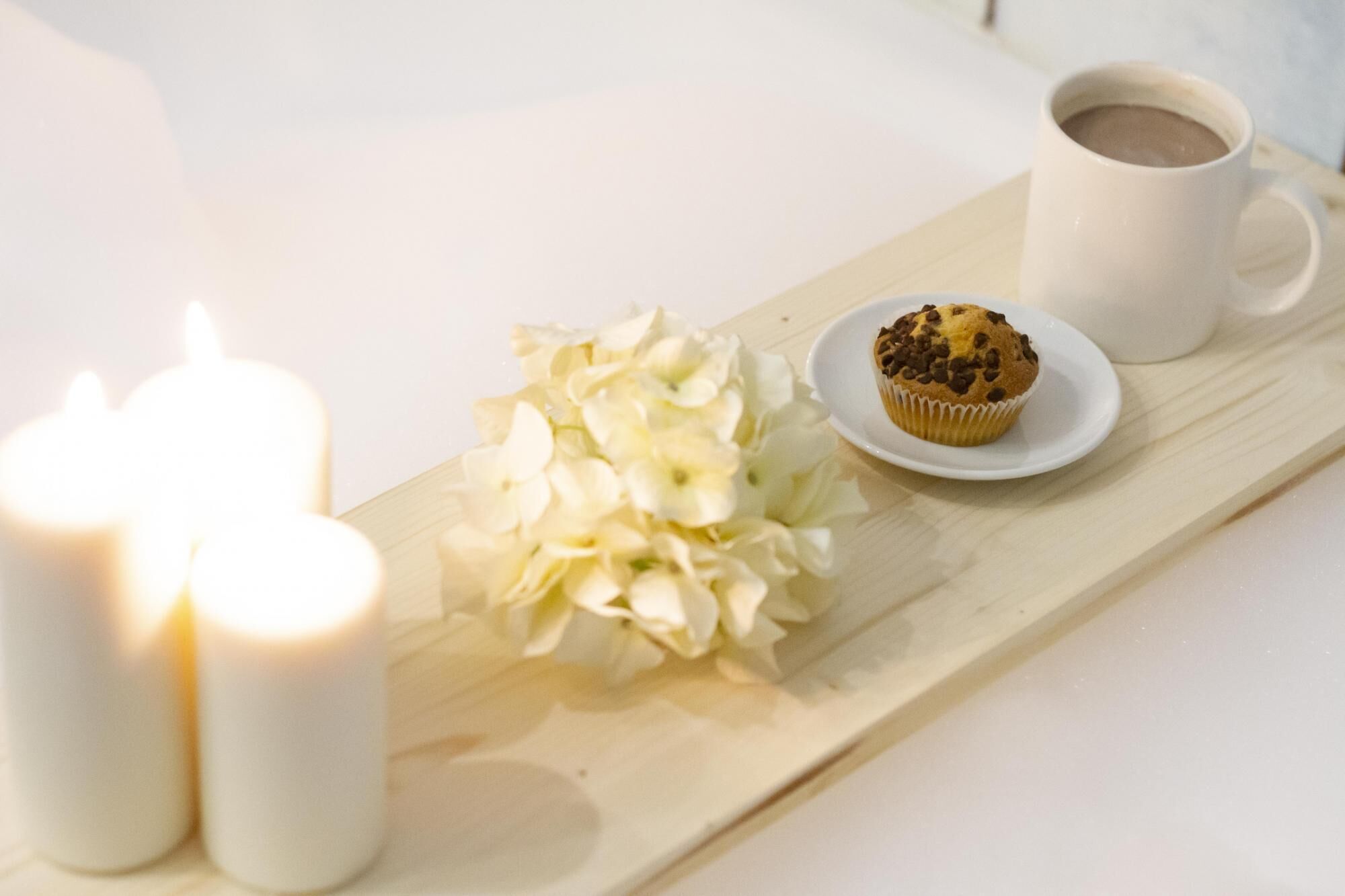 Ein Tablett mit einem Muffin, einer Tasse Kaffee und weißen Kerzen.