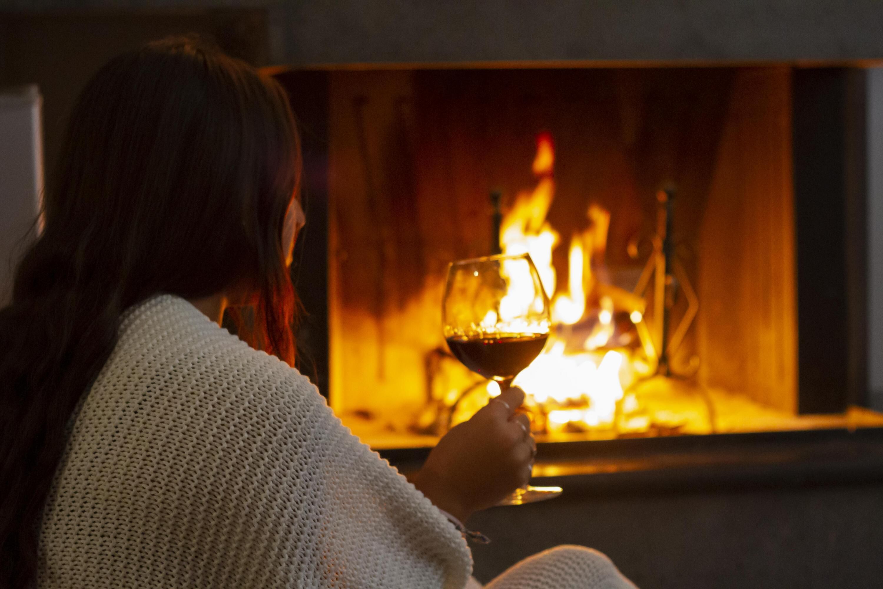 Eine Person sitzt am Kamin und hält ein Weinglas.