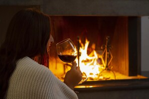 A person holding a glass of red wine in front of a fireplace.
