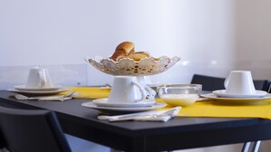 Taula de l'esmorzar amb una cafetera blanca, una tassa blanca, un bol de cereals i un plat blanc.