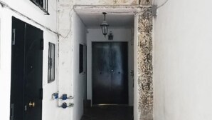 A narrow hallway with a black door on the left, a white wall with a blue pipe, and a dark door at the end. - Via Nilo 20 Appartamento Grande (Naples)