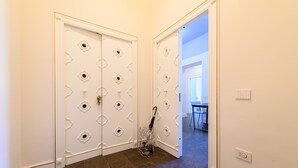 A hallway with a white door with decorative cutouts and a metal rack with an umbrella. - Corso Umberto 58 in Napoli (Naples)