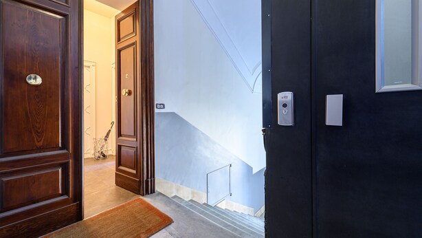 A wooden door with a brass handle, a dark-colored door next to it, and a staircase leading to an upper floor. - Corso Umberto 58 in Napoli (Naples)