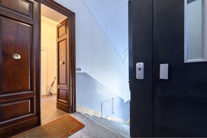 Eine Holztür mit Messingklinke, daneben eine dunkle Tür und eine Treppe, die zu einer oberen Etage führt.