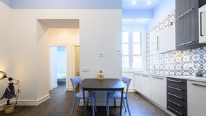 A modern kitchen with a dark countertop, white cabinets, and a patterned backsplash. There is a dining table with blue chairs and a small decorative item on it. - Corso Umberto 58 in Napoli (Naples)
