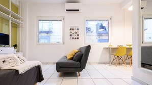 Ett modernt rum med en grå soffa, ett matbord med gula stolar och en tv-apparat placerad på ett vitt skåp.