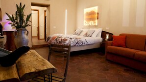 A bedroom with a bed, a wooden chair, a sofa, a potted plant, and a wall-mounted artwork. - Napolicentrico in Napoli (Naples)