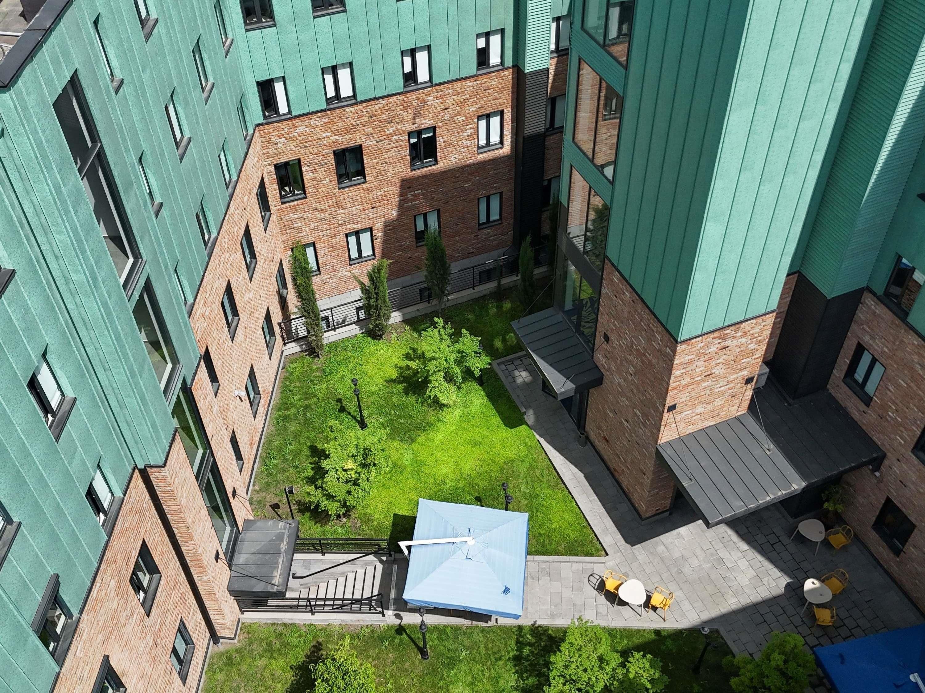 Un edificio a più piani con un cortile che presenta una struttura con tetto blu, posti a sedere all'aperto e una scala che conduce ai piani superiori.