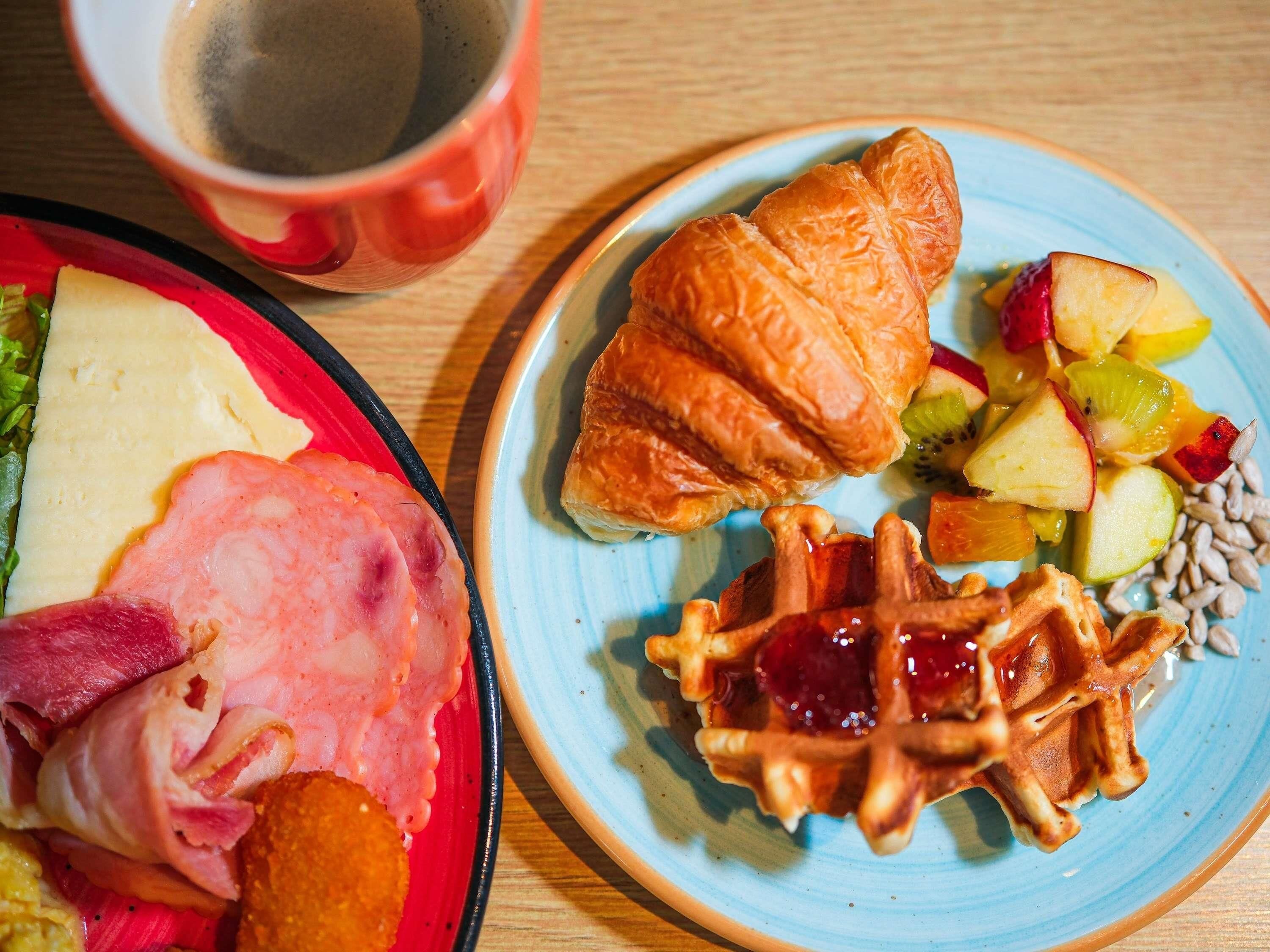 A breakfast plate with ham, eggs, and toast, and a plate with a croissant, fruit, and waffles.