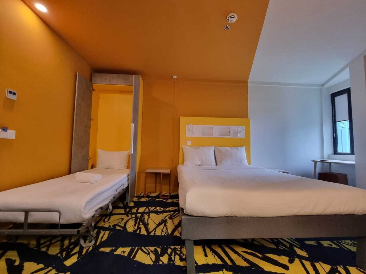 Una camera d'albergo con due letti singoli, un tavolino, una panca e una finestra.