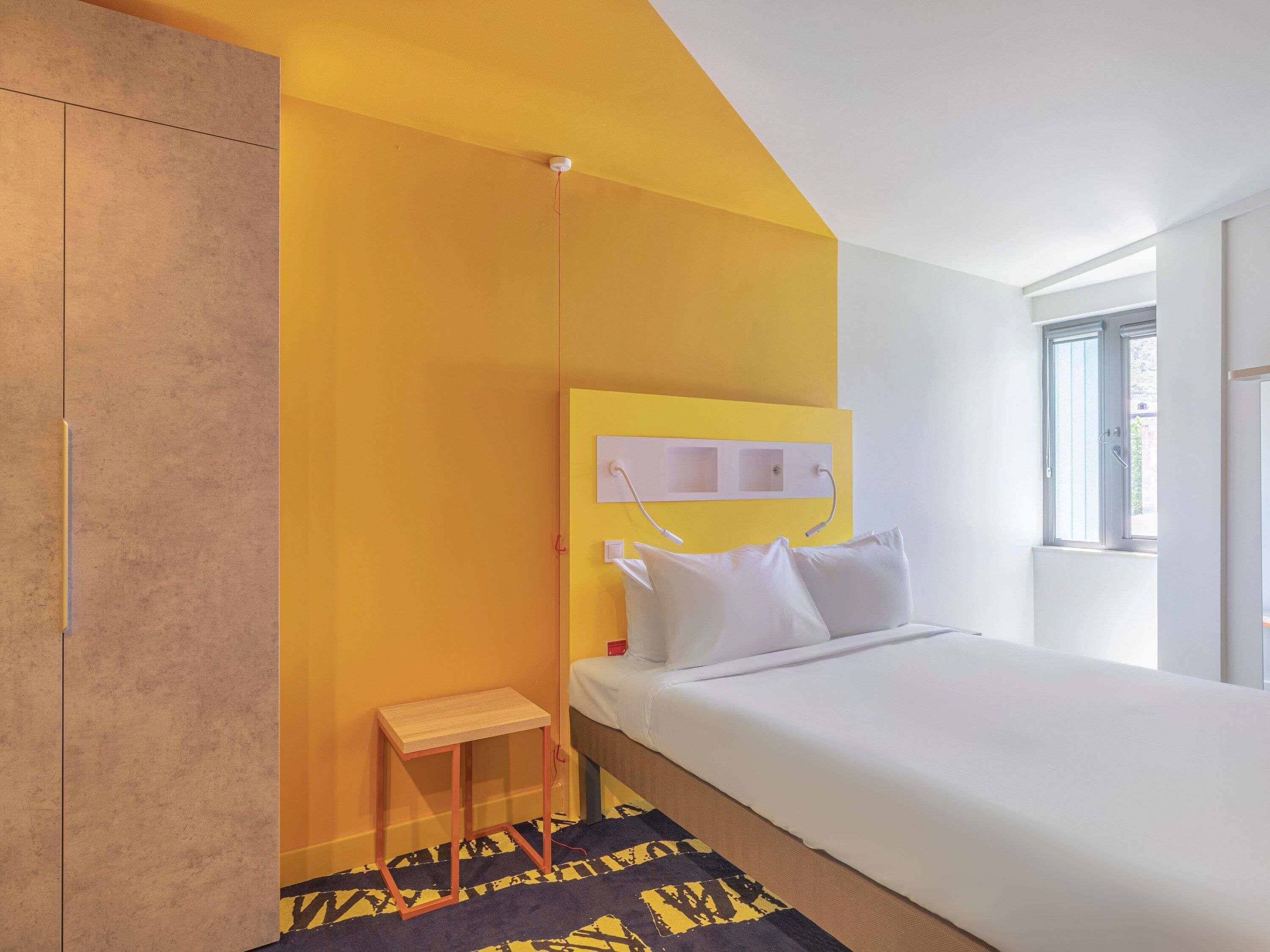 A hotel room with a bed, a small table, a wardrobe, and a window.