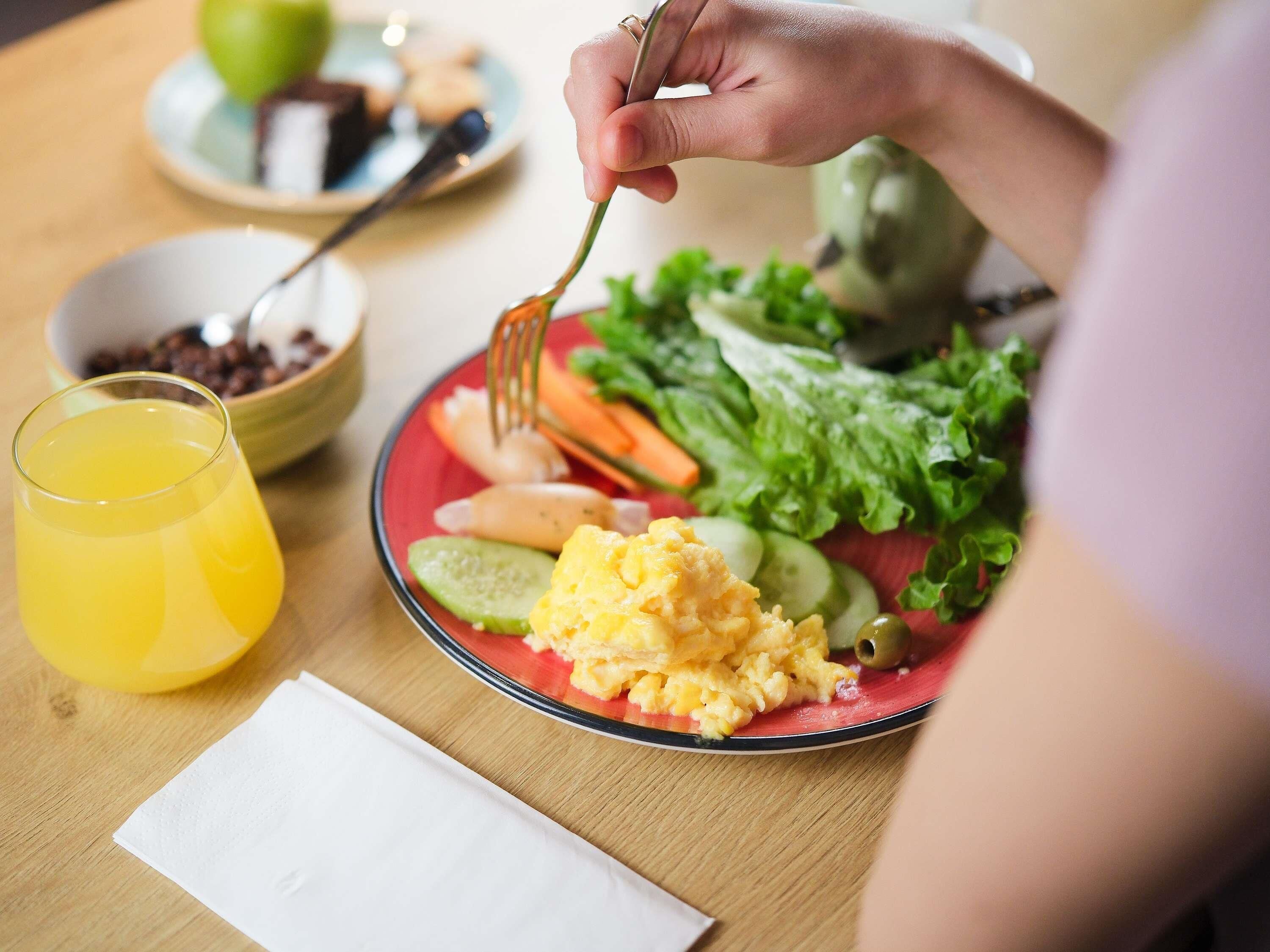 Una mesa de comedor con un plato de huevos revueltos, verduras y un vaso de jugo de naranja.