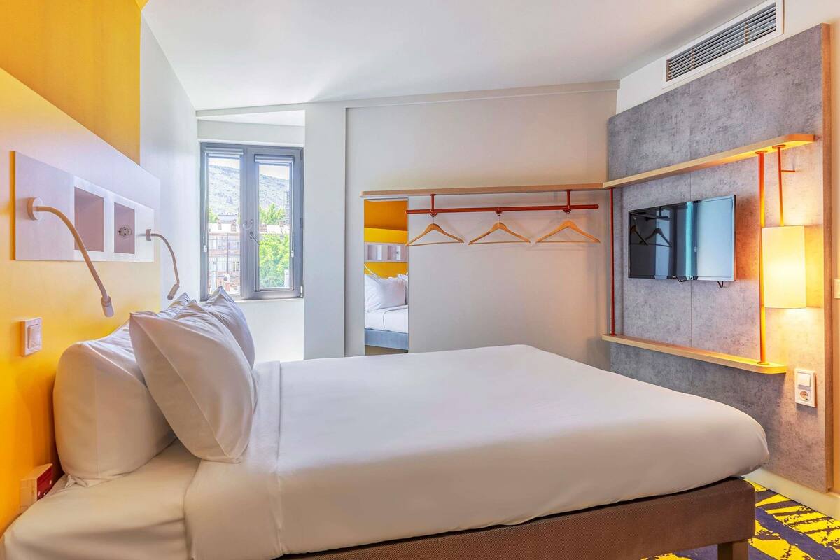 A hotel room with a bed, a TV, a wardrobe, and a window.