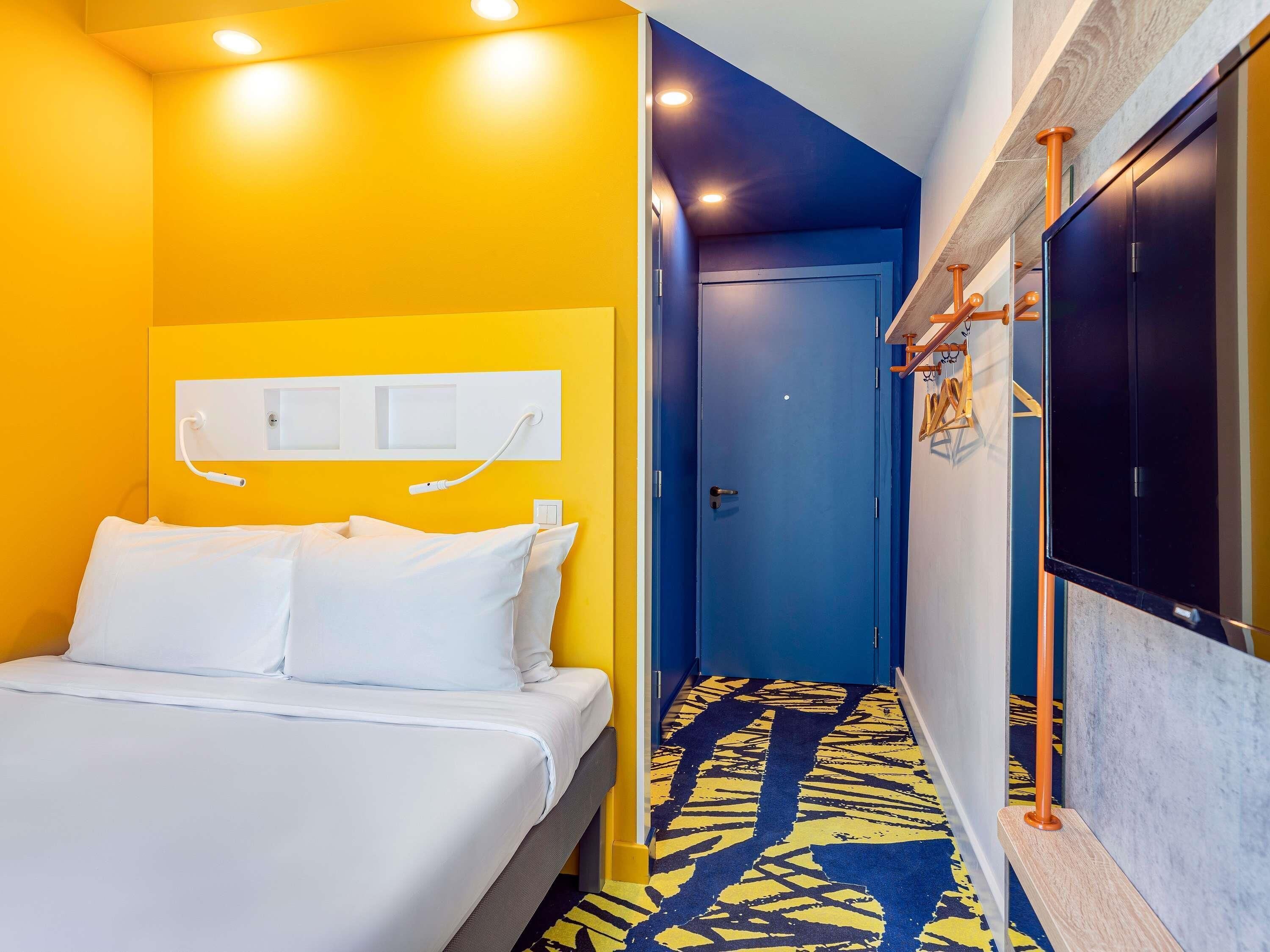 Habitación de hotel con una cama, una puerta azul y una alfombra estampada.