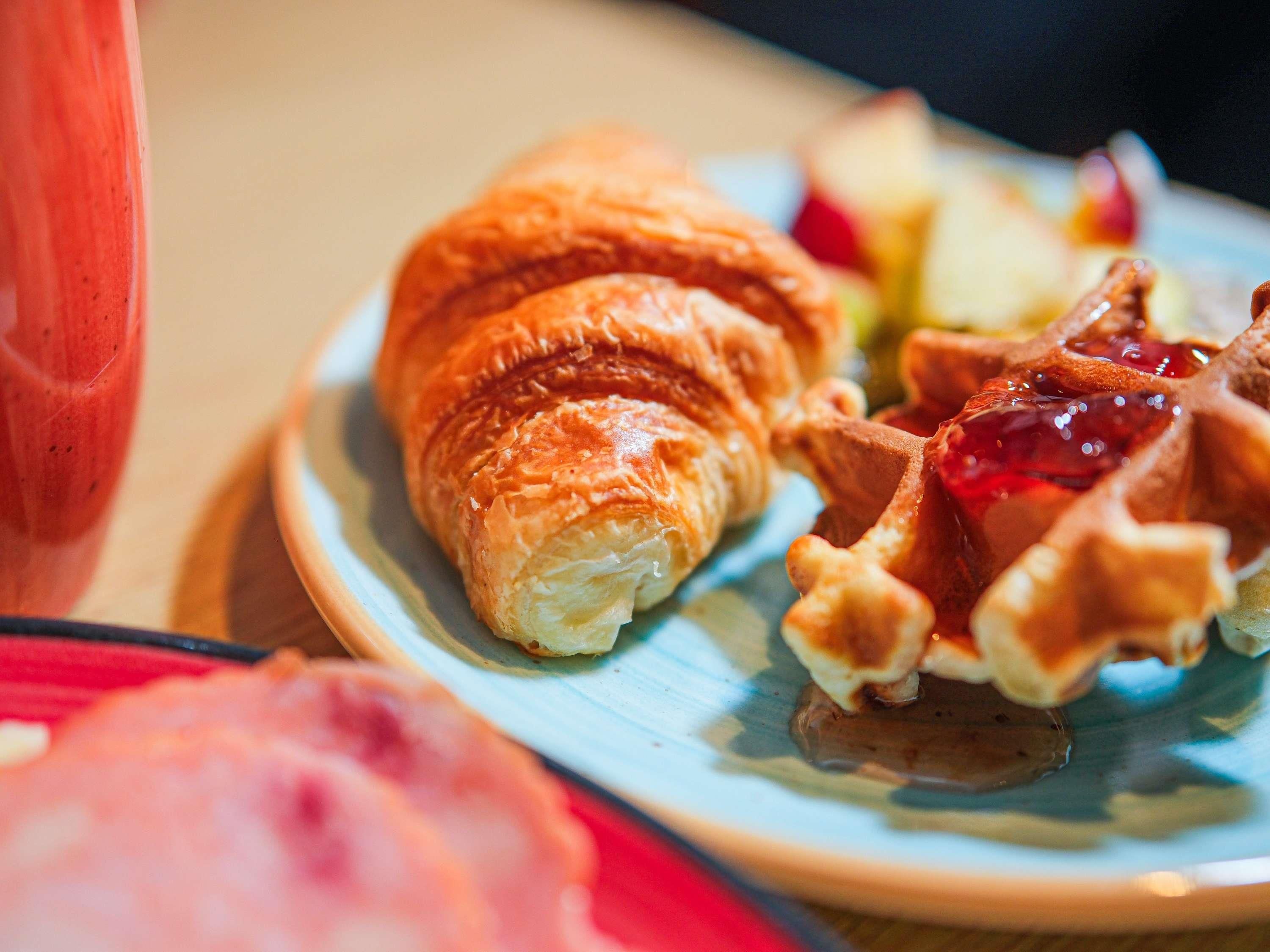A plate with a croissant and a waffle, and a glass of a red beverage.