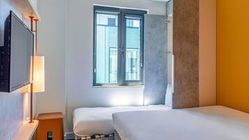 A hotel room with a bed, a TV, a window, and a small table.
