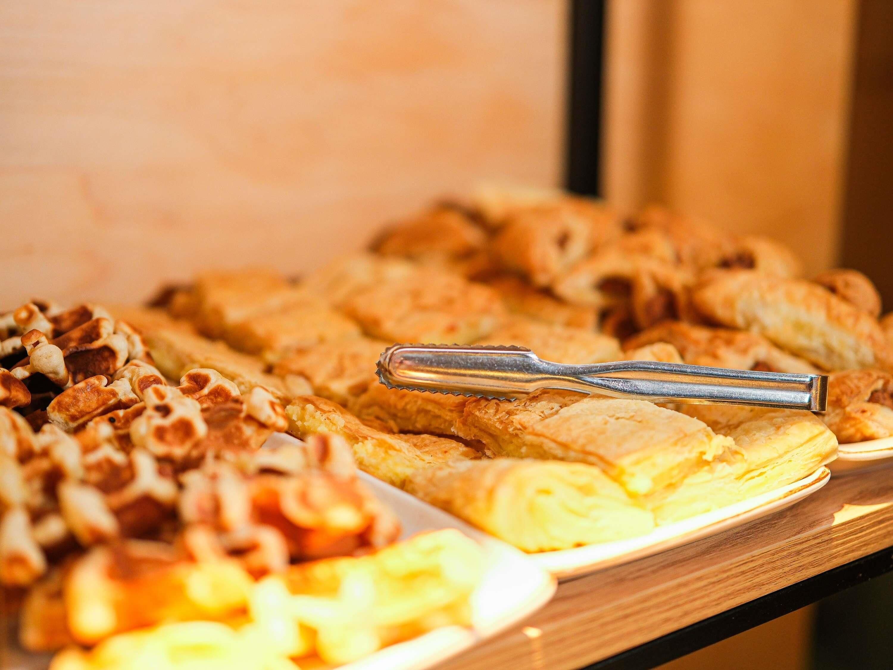 A buffet table with various pastries and a pair of tongs.