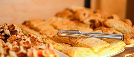 A buffet table with various pastries and a pair of tongs.