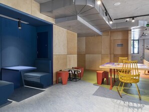 Un intérieur moderne avec un coin salon bleu, une table entourée de chaises jaunes et un mélange de murs en bois et en béton.