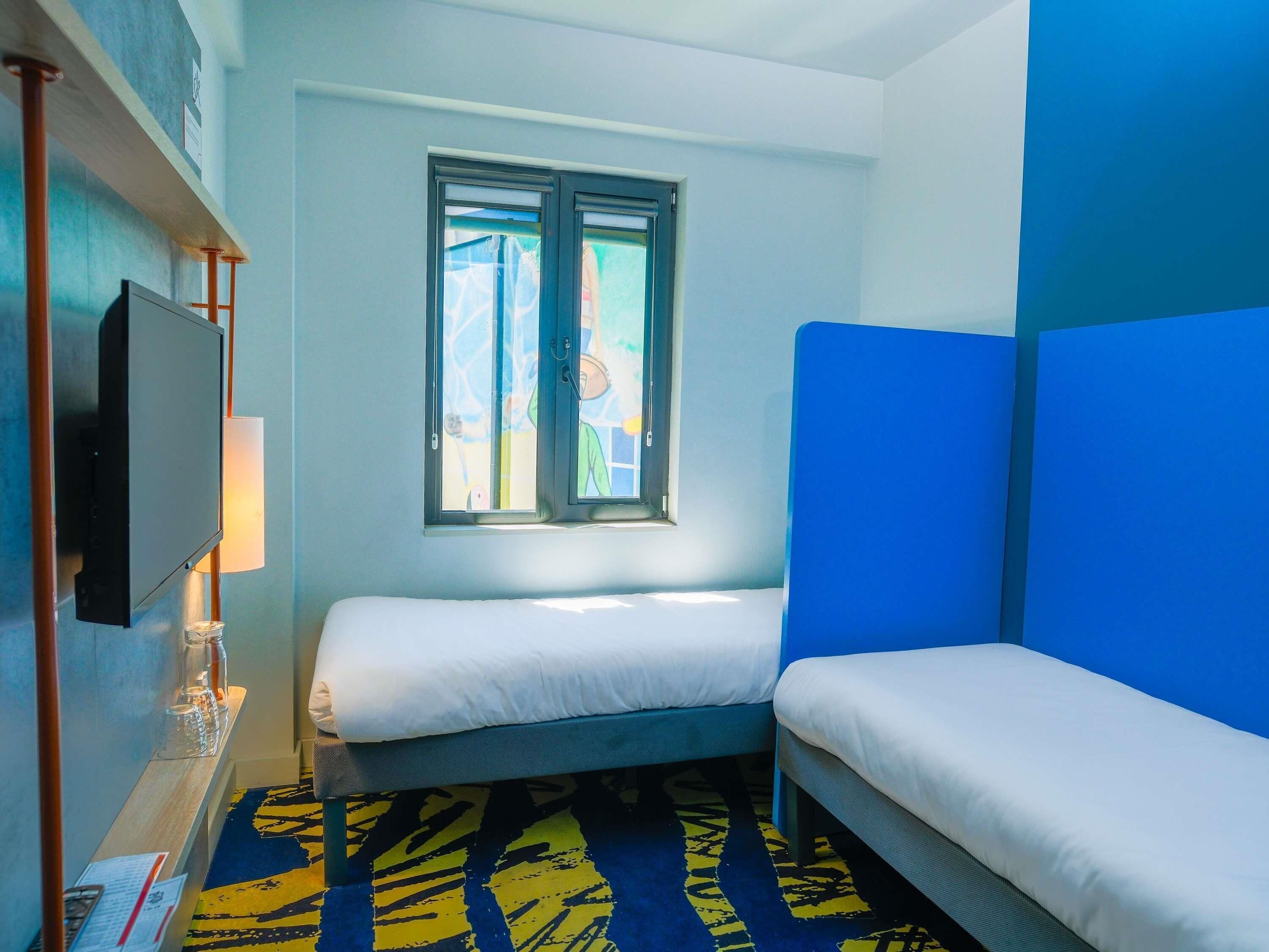 Une petite chambre moderne, équipée d’un lit, d’une télévision et d’une fenêtre.