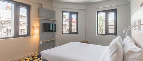 Una habitación de hotel con cama, televisión y ventana con vista a edificios.