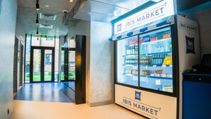 A corridor with a glass door leading to an outdoor area, a vending machine, and a refrigerated display case labeled 'IBIS MARKET'. - Ibis Budget Tbilisi Center (Tbilisi)