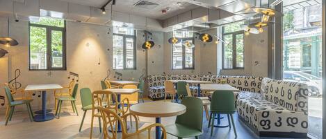 A modern cafe with round tables, green and yellow chairs, and a patterned sofa.
