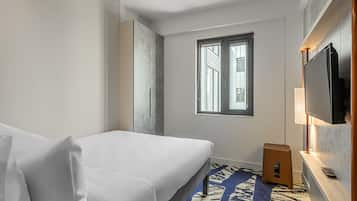 Habitación de hotel con cama, televisor, ventana y un taburete pequeño.