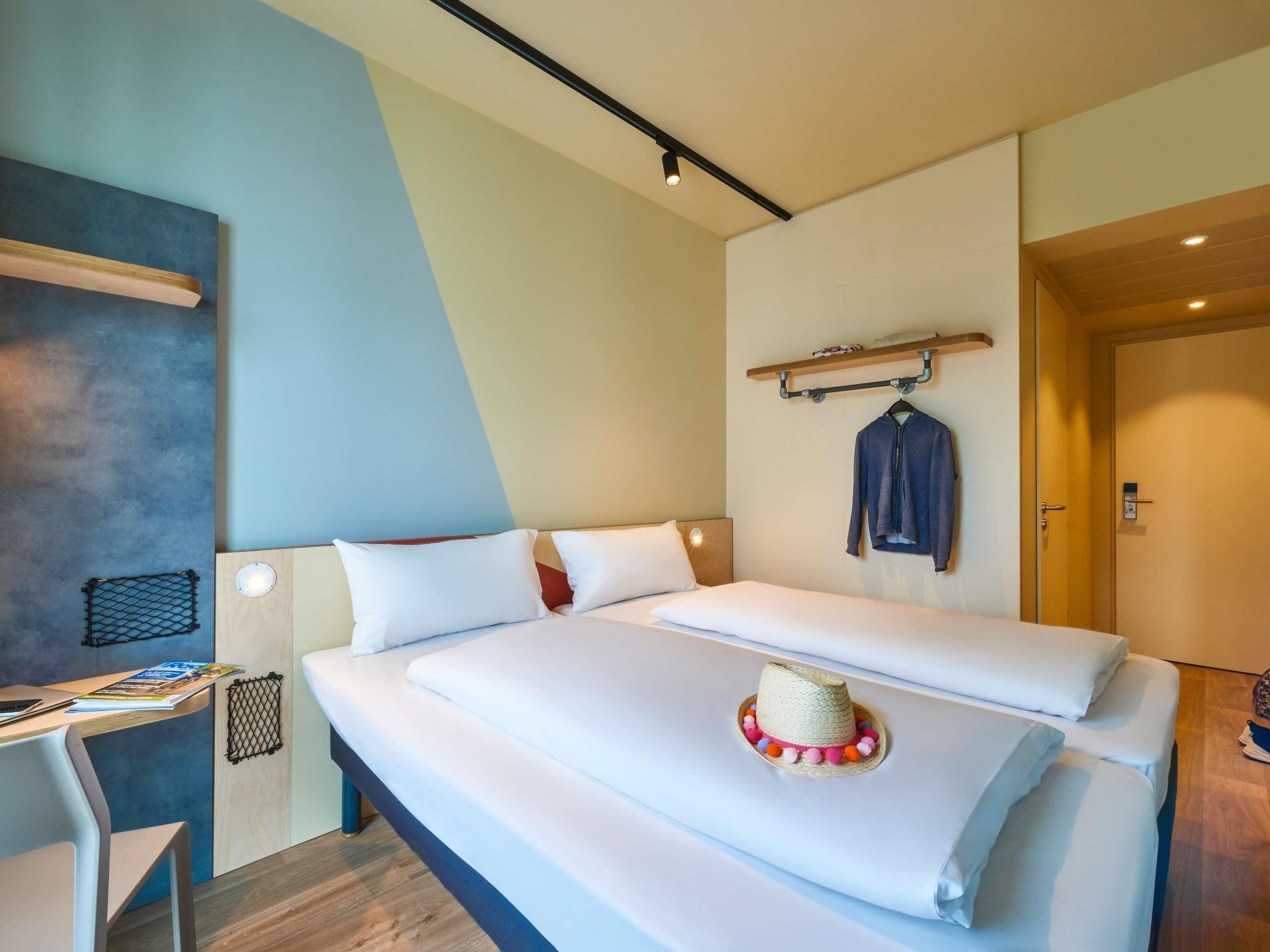 A modern hotel room with a bed, a desk, and a hanging coat rack.