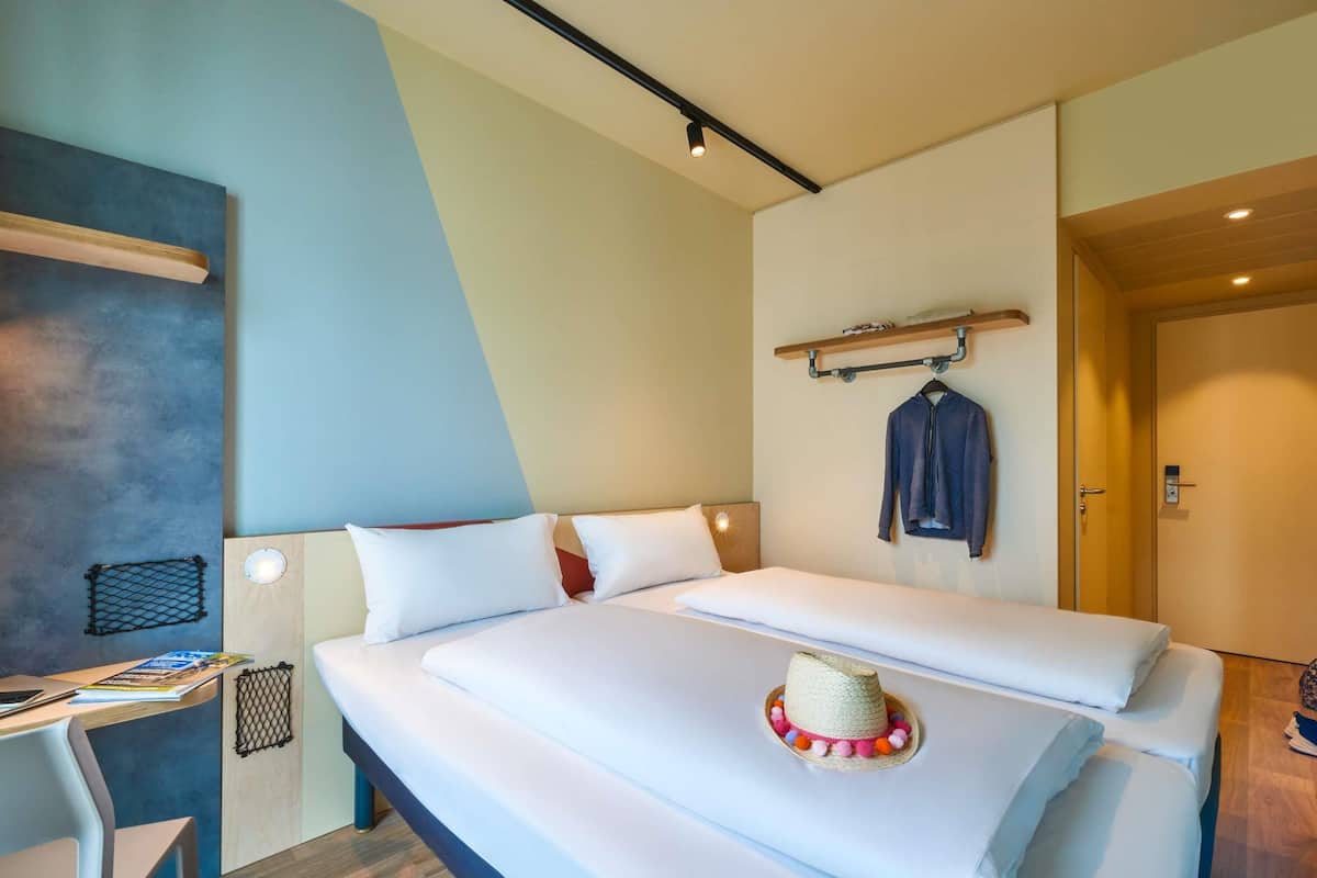 A modern hotel room with a bed, a desk, and a hanging coat rack.