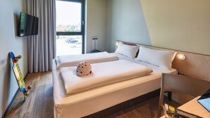 A hotel room with a bed, a TV mounted on the wall, a suitcase, and a skateboard leaning against the wall. - Ibis Budget Singen (Singen)