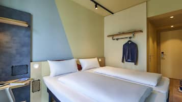 A hotel room with a bed, a desk, and a coat rack.