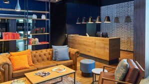 A modern lounge area with leather sofas, a wooden reception desk, and bookshelves filled with books. - Ibis Budget Singen (Singen)