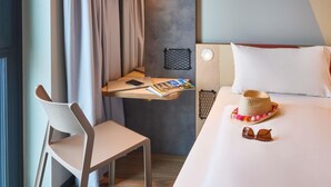 A hotel room with a bed, a desk with a laptop, a chair, and a bedside table with a hat and sunglasses. - Ibis Budget Singen (Singen)