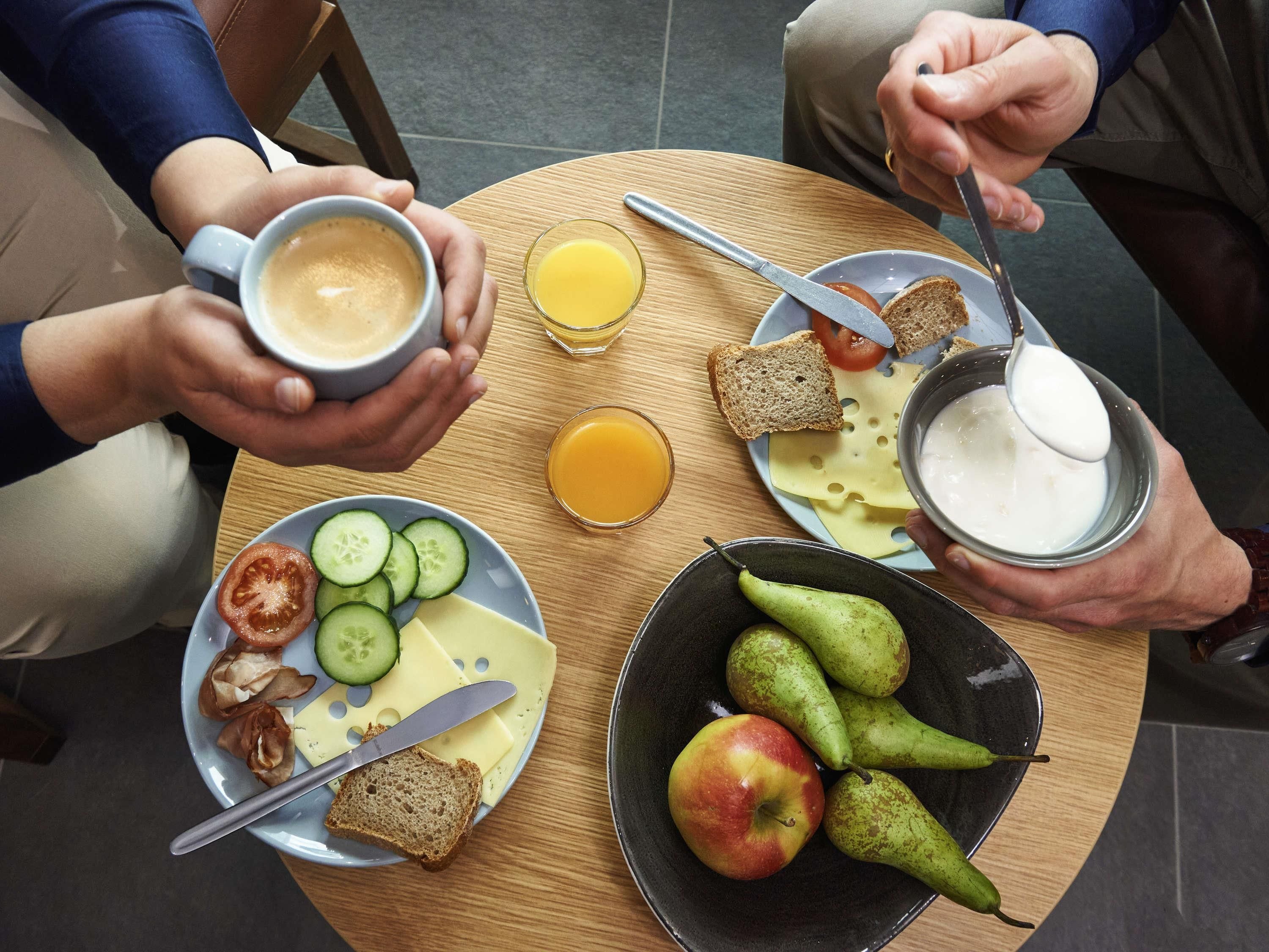 A table with food items and drinks, including bread, cheese, tomatoes, cucumbers, pears, an apple, and a cup of coffee.