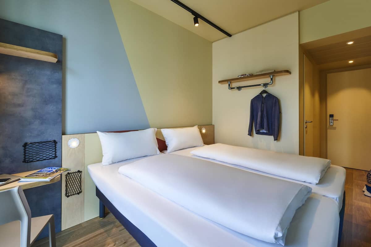 A hotel room with a bed, a desk, and a coat rack.